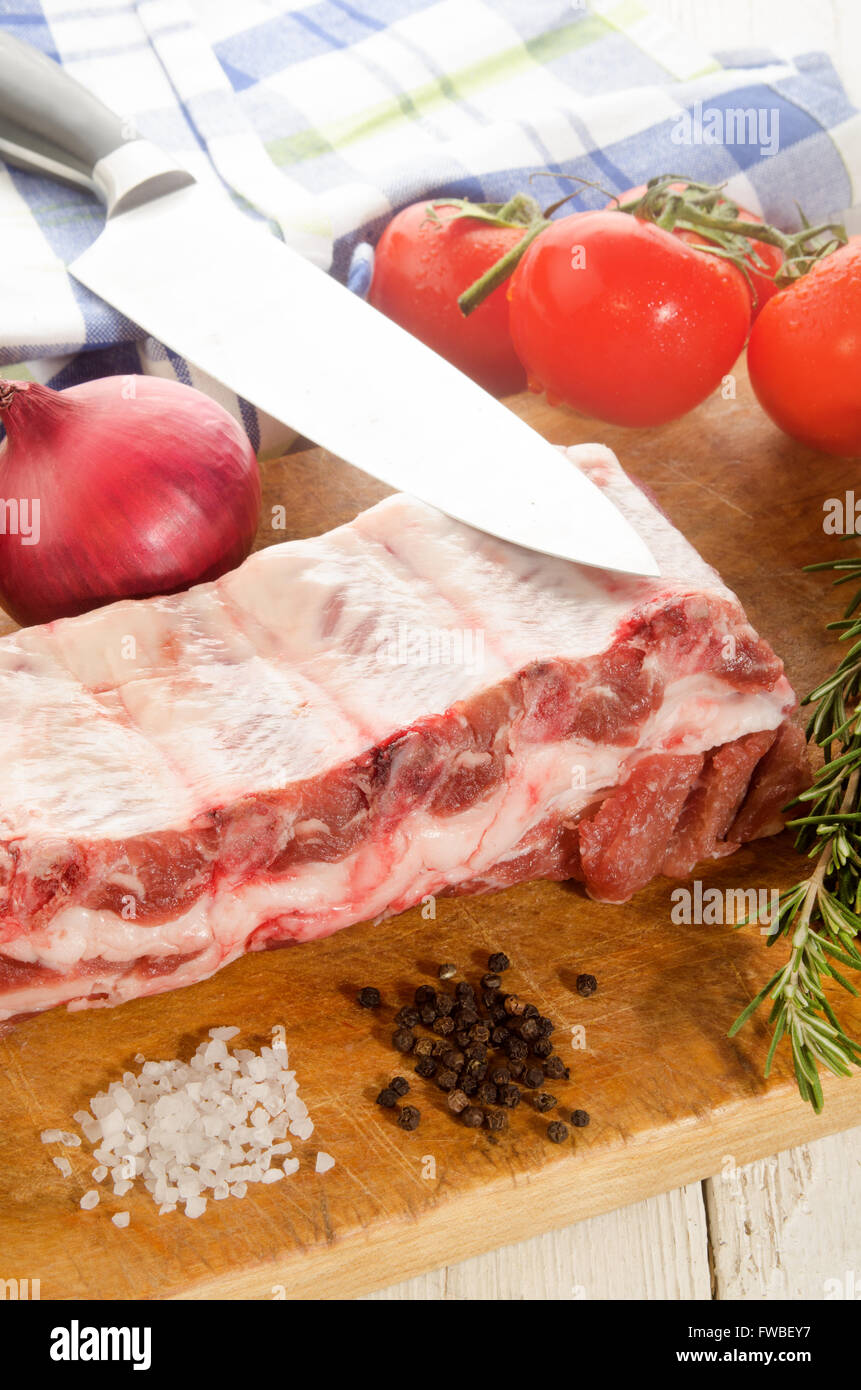 Materie costolette di maiale con cipolla, pomodoro, rosmarino, sale grosso e pepe nero su pannello di legno Foto Stock