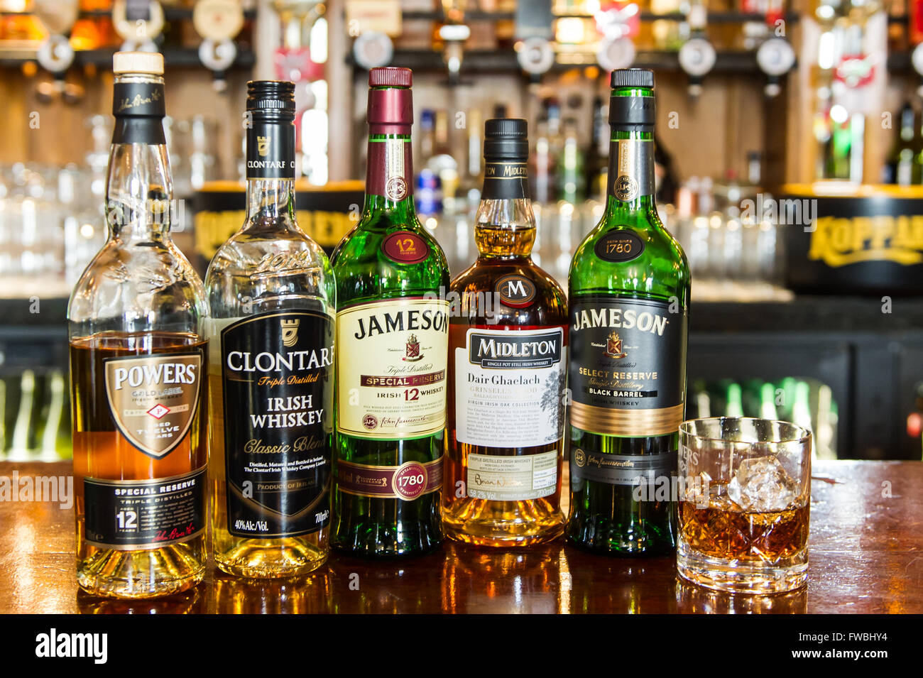 5 bottiglie di whisky e un bicchiere di whiskey con cubetti di ghiaccio su un banco di bar top in Irlanda. Foto Stock