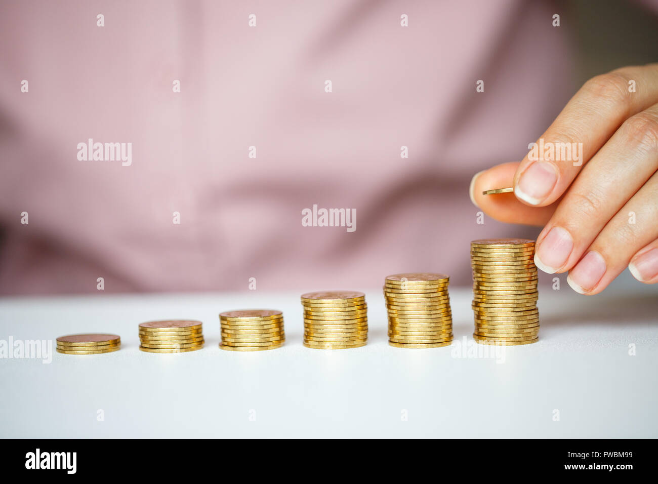 Risparmio di mano femminile di impilamento delle monete in oro in colonne crescente Foto Stock