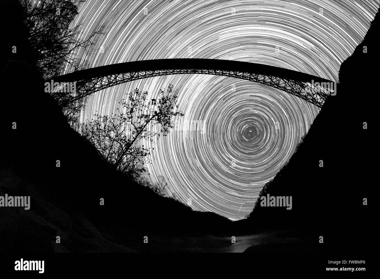 Il movimento delle stelle appendere congelati in cielo al di sotto di un arco gigantesco ponte in acciaio su una gola in bianco e nero, New River Gorge, West Virginia. Foto Stock
