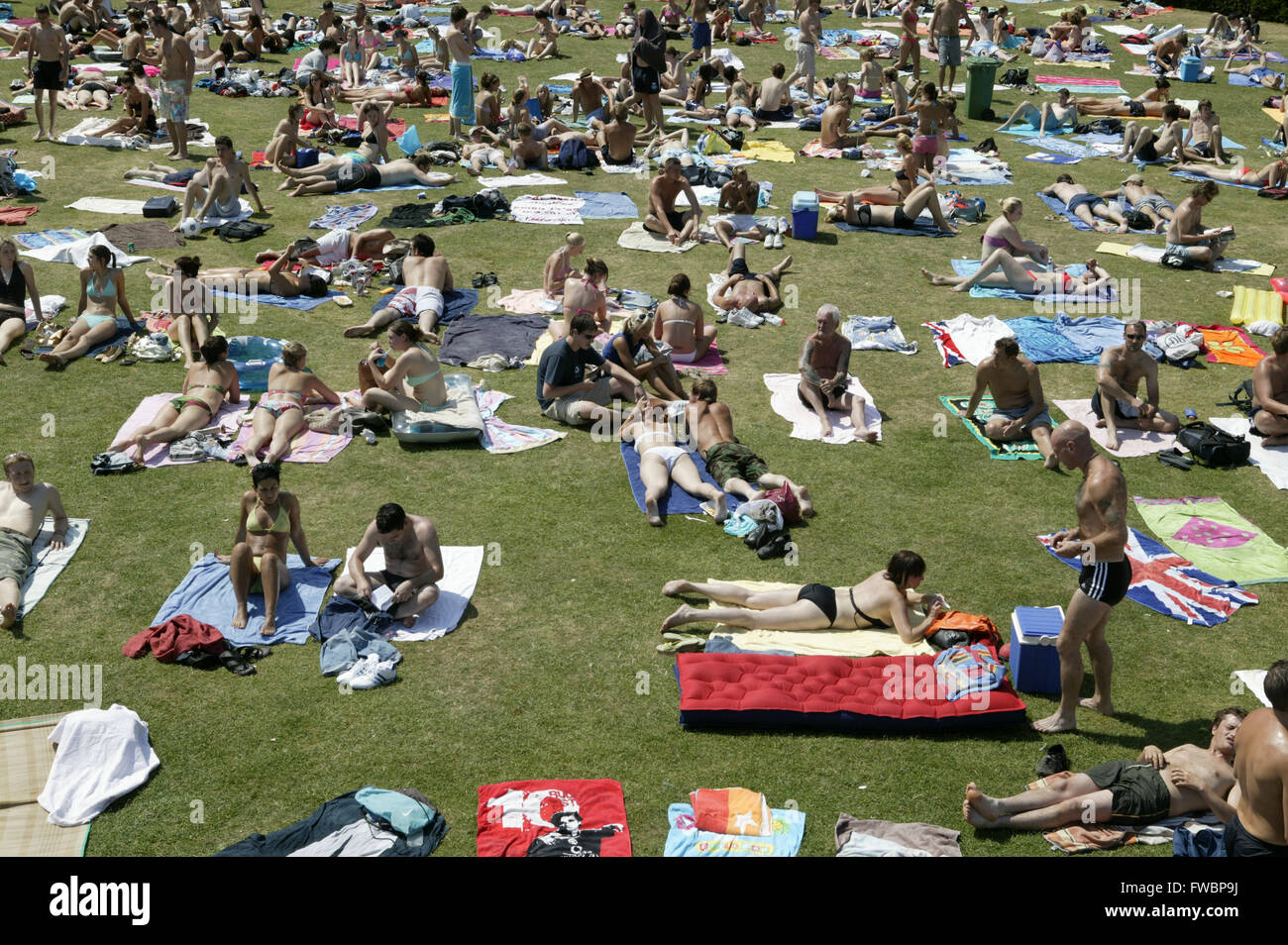 Canicola estiva e persone rinfrescarvi all'ombra e laici la cottura in sun dal lato di un pranzo di piscina all'aperto a Cheltenham, Regno Unito. Foto Stock