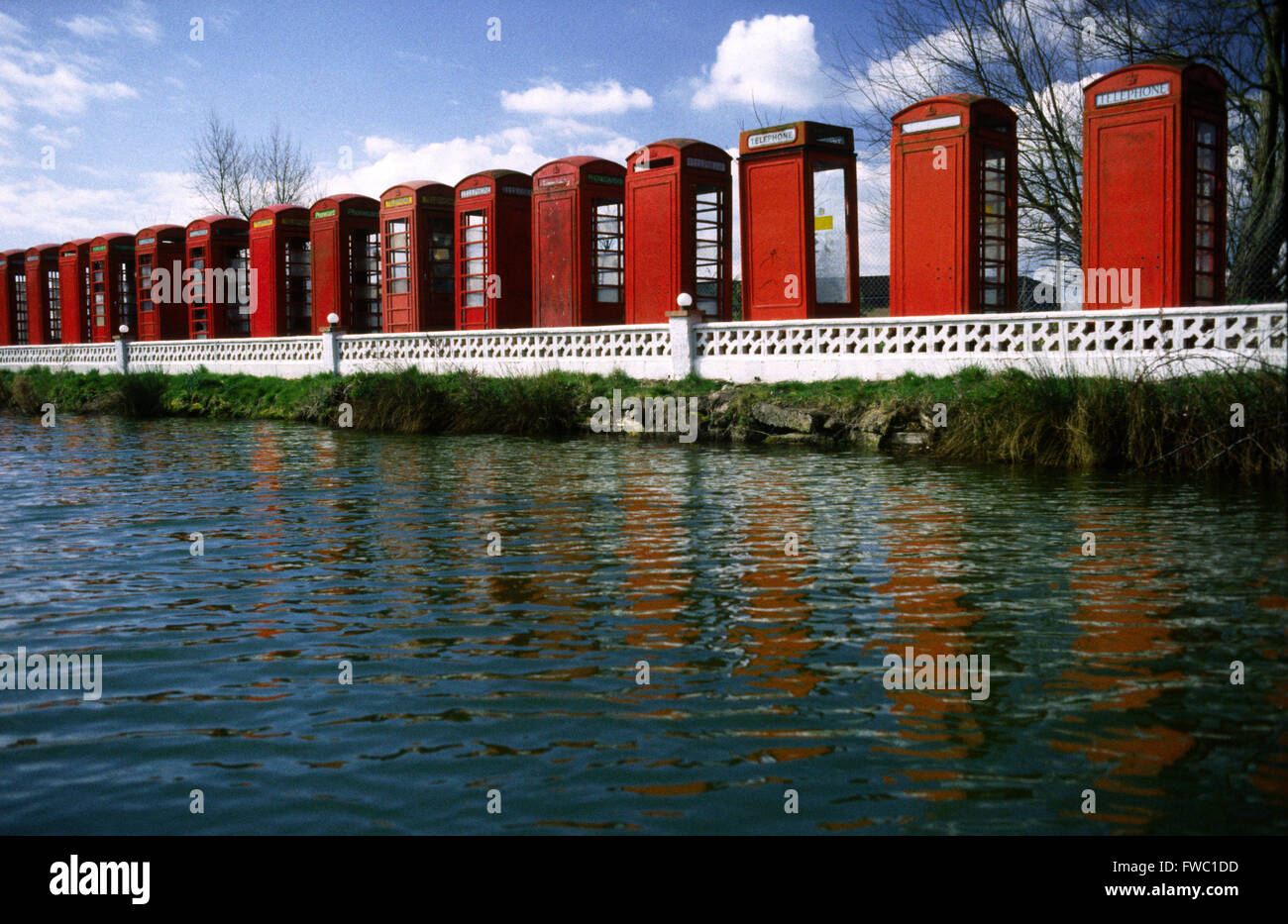 Raccolta di scatole telefoniche rosse allineate e adagiato sul bordo di un laghetto che riflette il colore e la forma dell'acqua. Foto Stock