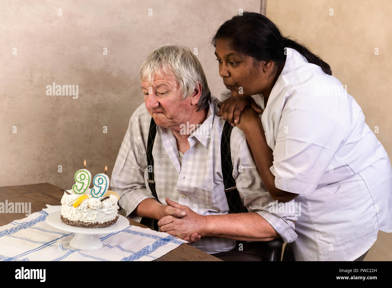 Uomo anziano in casa di cura soffiando le candeline sulla sua torta di compleanno Foto Stock