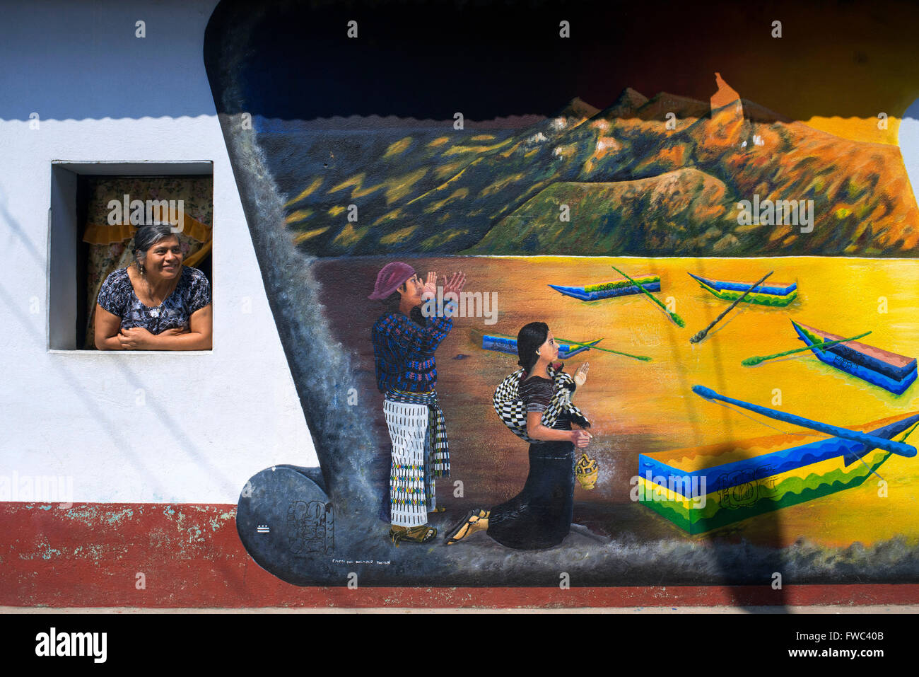 Donna locale in un windows accanto a un muro dipinto in San Juan La Laguna, Sololá, Guatemala. Tradizione maya arte pittura Sant Foto Stock