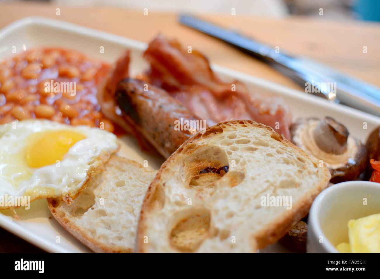 Colazione cucinata con toast, pancetta, uova fritte, salsicce, fagioli al forno, i funghi e il burro - filtro applicato Foto Stock