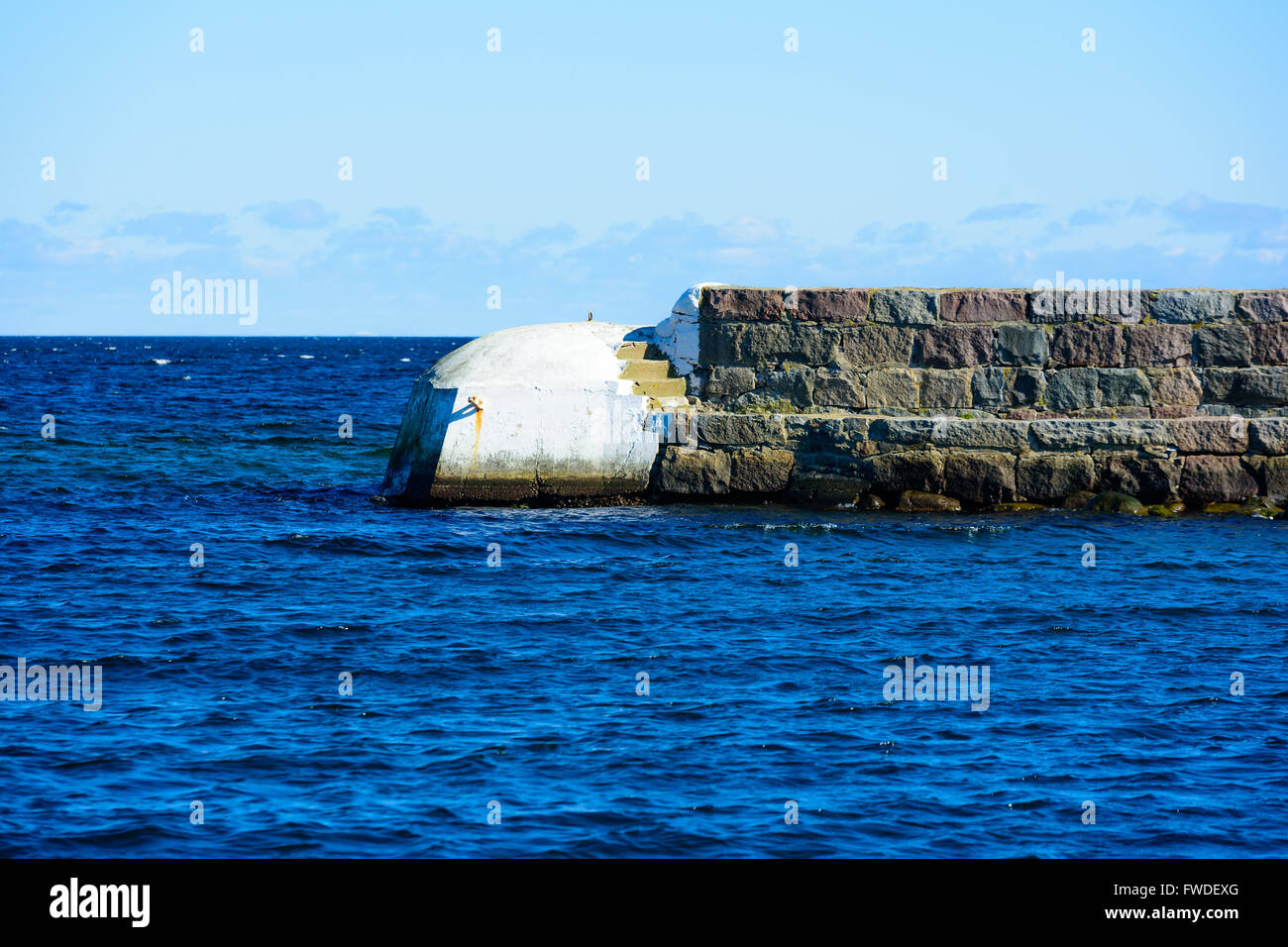 L'estremità bianca di una pietra e il molo di cemento con il mare aperto in background. Foto Stock
