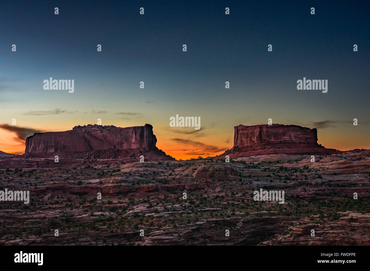 Il sole tramonta dietro il gigante formazioni rocciose, Monitor e Merrimac buttes trovata nel midwest America, Utah. Foto Stock