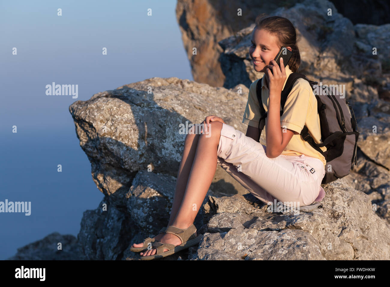 Sorridente giovane donna parla al telefono e seduta su di una pietra sulla montagna Foto Stock