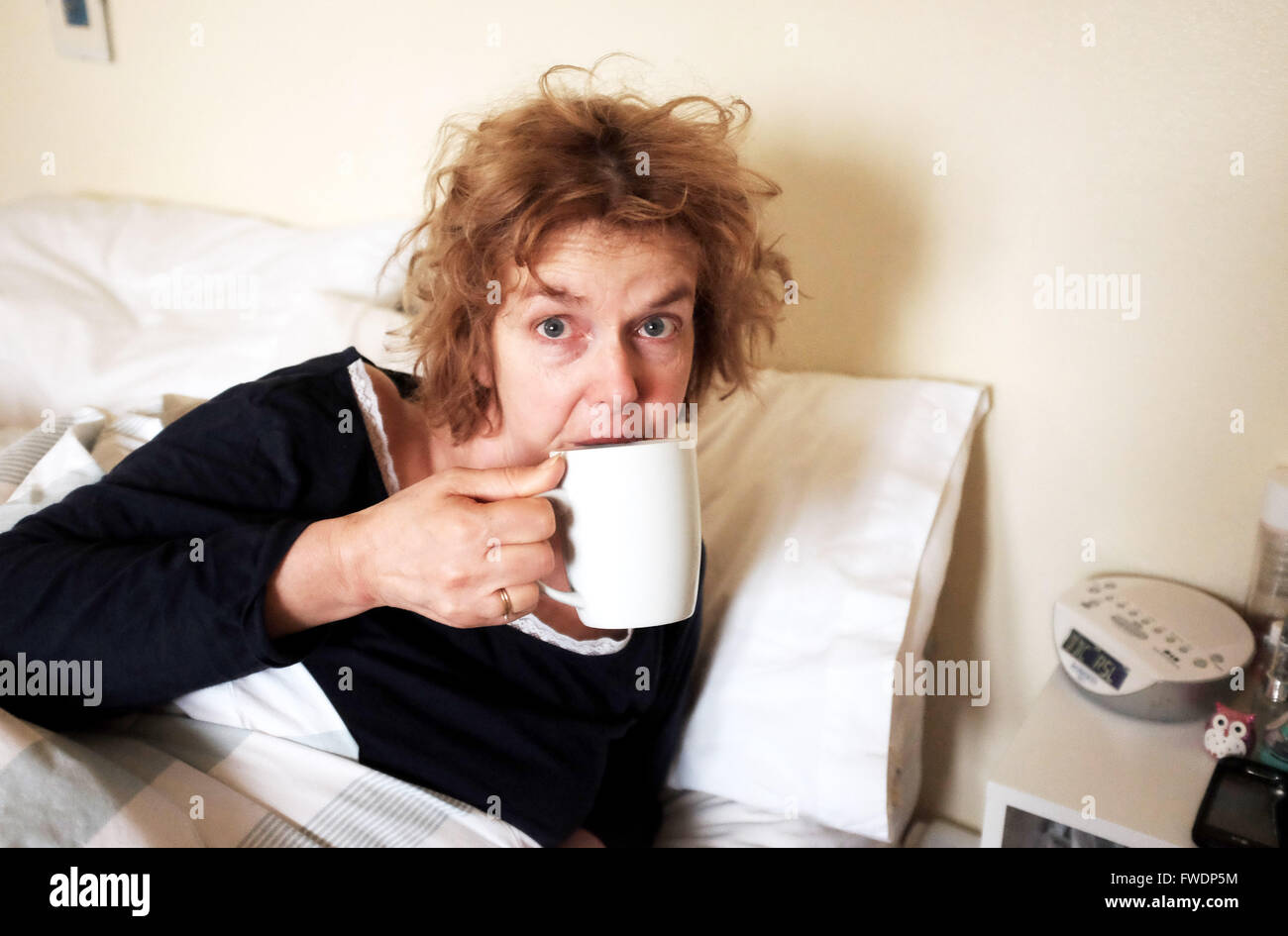 Donna che guarda disheveled bicchiere di tè dopo il risveglio al mattino a letto Foto Stock