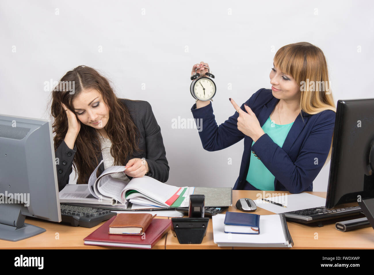 Due ragazze in ufficio in attesa della fine del giorno e guardare l'orologio Foto Stock