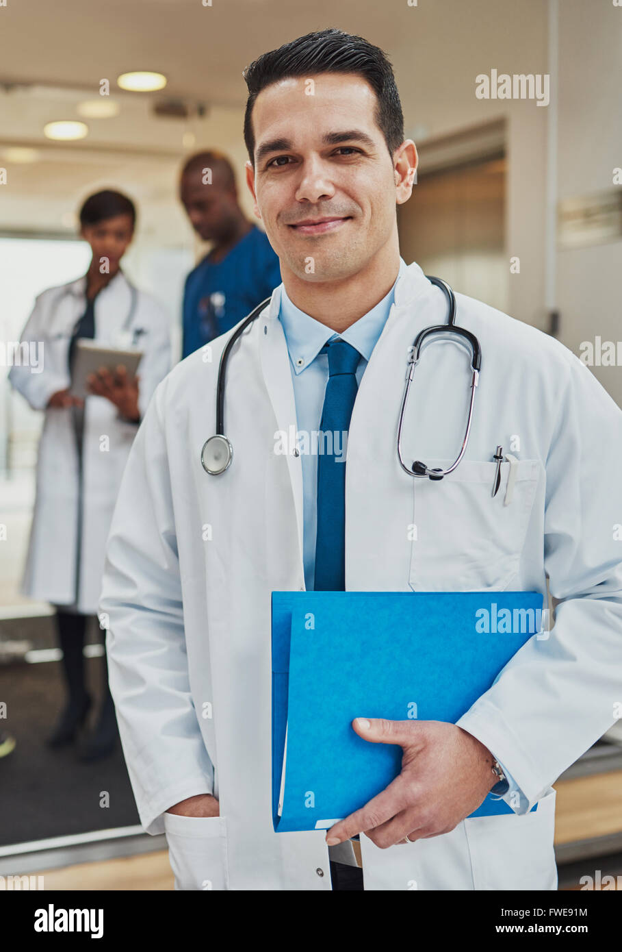 Gentile fiducioso ispanico medico con un file del paziente nelle sue mani indossando un camice e stetoscopio guardando la telecamera wit Foto Stock