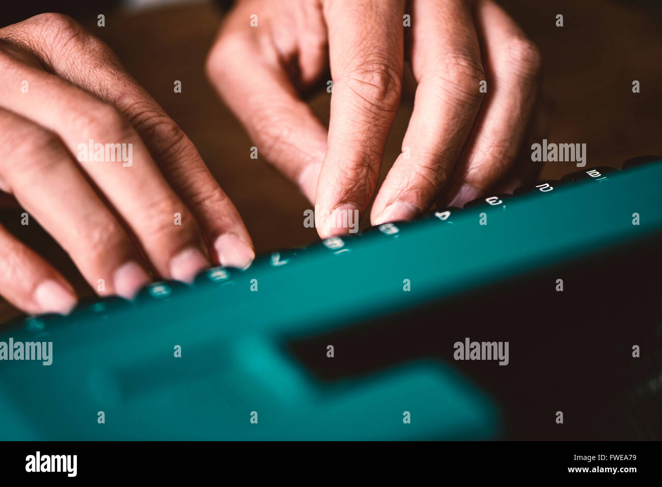 Primo piano delle mani di un giovane uomo di digitazione in una vecchia macchina da scrivere blu Foto Stock