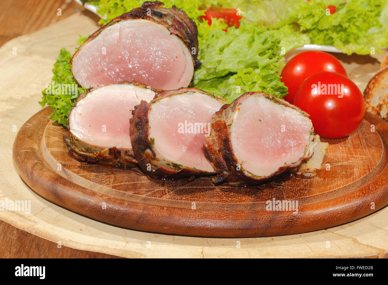 Filetto di maiale, medaglioni, carne avvolti in pancetta, grigliate e guarnita con lattuga e pomodoro su una tavola di legno Foto Stock