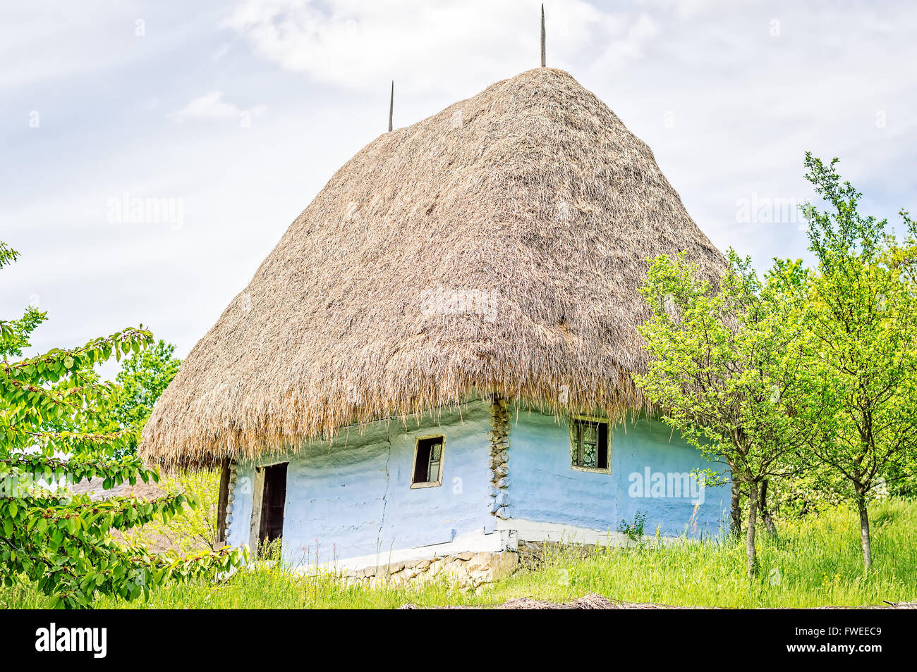 Luce blu vecchia casa di argilla con il tetto di paglia, travi in legno e pietra di fondamento. Foto Stock