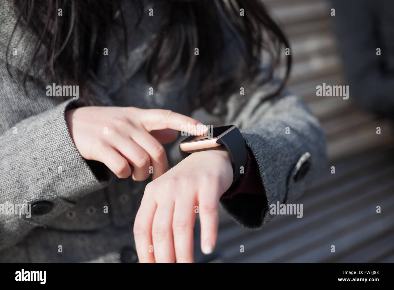 Le mani di una donna in cappotto grigio navigando il suo moderne smart watch. Questa persona è sempre collegato al social media e internet Foto Stock
