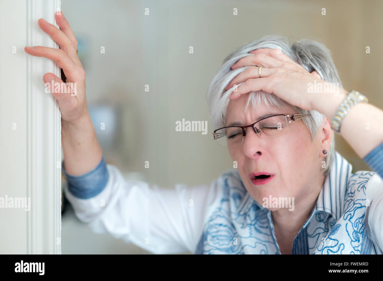 Senior donna con un mal di testa trattiene la sua mano sulla fronte e puntelli se stessa sul telaio della porta, Germania Foto Stock
