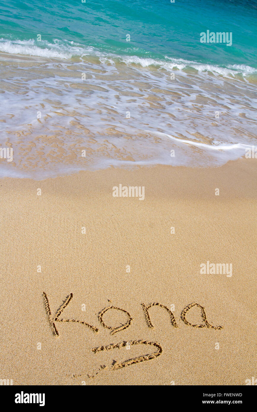 Questa vacanza immagine mostra la parola Kona scritto nella sabbia con l'oceano onde di acqua in arrivo per lavare la scrittura di distanza. Foto Stock