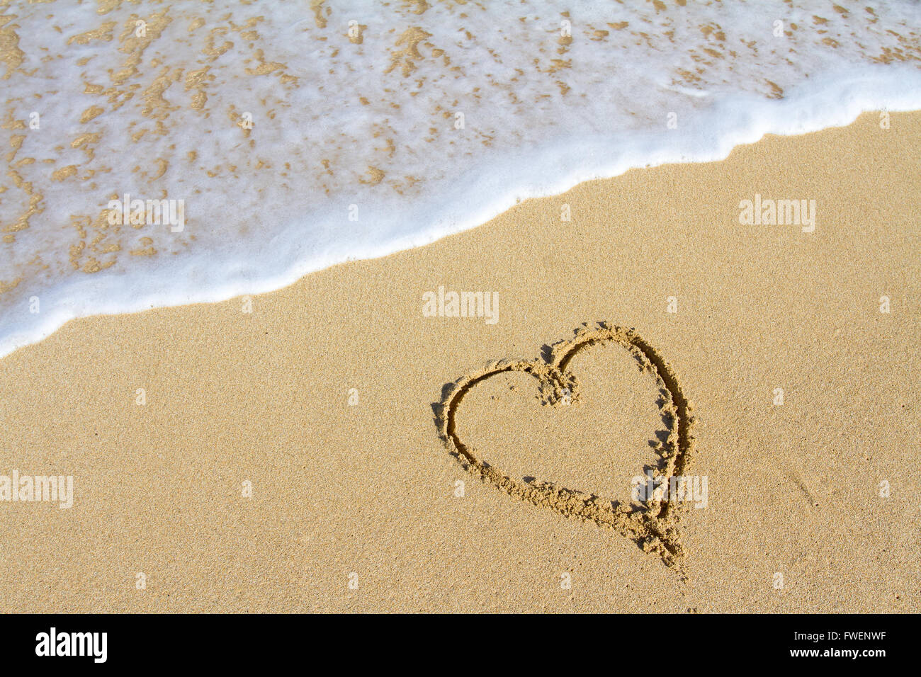 Un cuore è disegnato nella sabbia sulla spiaggia delle Hawaii che mostra un'immagine di sabbia bianca, acqua, le onde e il simbolo per l'amore. Questo wou Foto Stock