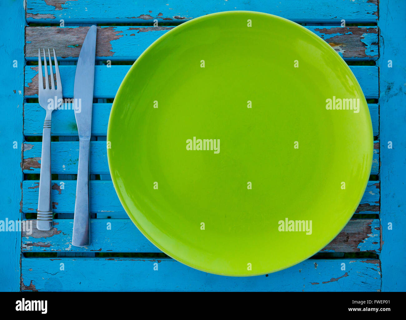 Un vuoto piastra verde su un weathered tavolo blu lungo con una forchetta e coltello si trova pronto per essere servito un pasto per mangiare. Foto Stock