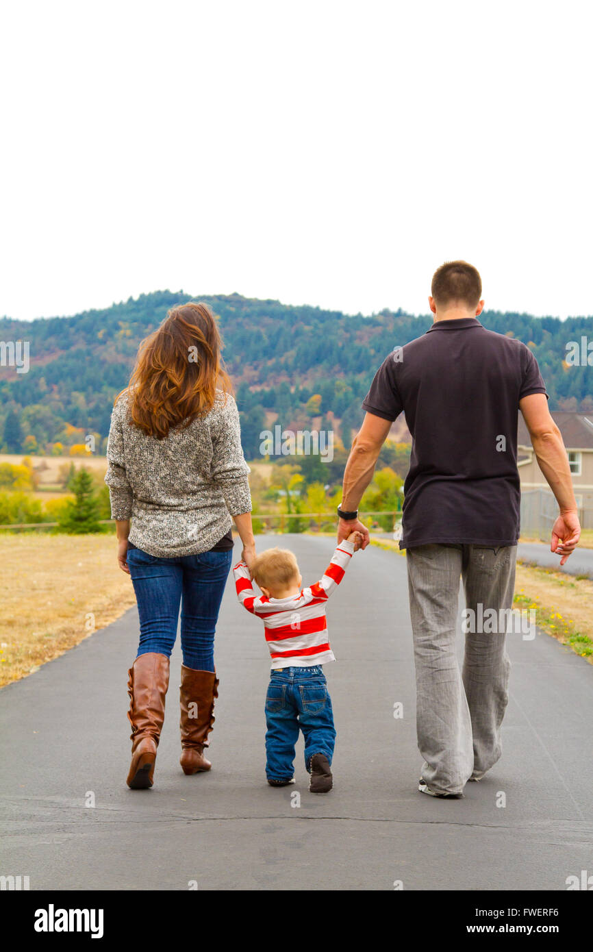 Una famiglia si allontana su un percorso tenendo le mani con il bambino nel mezzo. Foto Stock