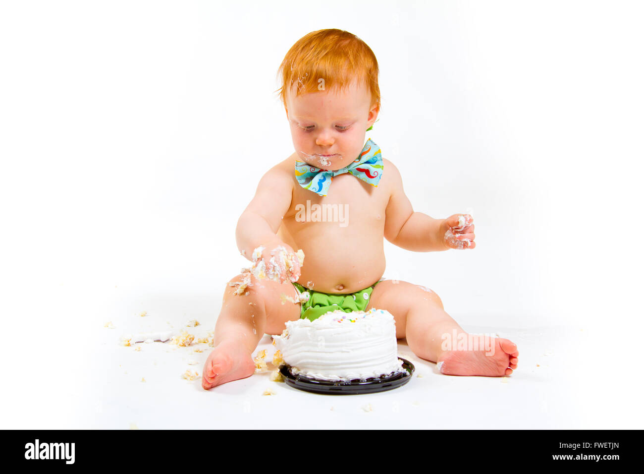 Un bambino arriva a mangiare la torta per la prima volta il suo primo compleanno in questa torta smash in studio contro uno sfondo bianco. Foto Stock
