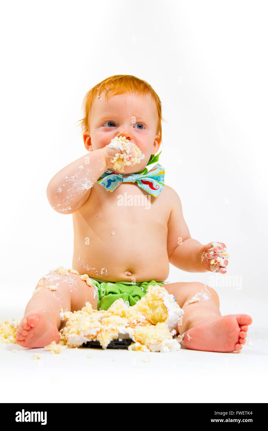 Un bambino arriva a mangiare la torta per la prima volta il suo primo compleanno in questa torta smash in studio contro uno sfondo bianco. Foto Stock
