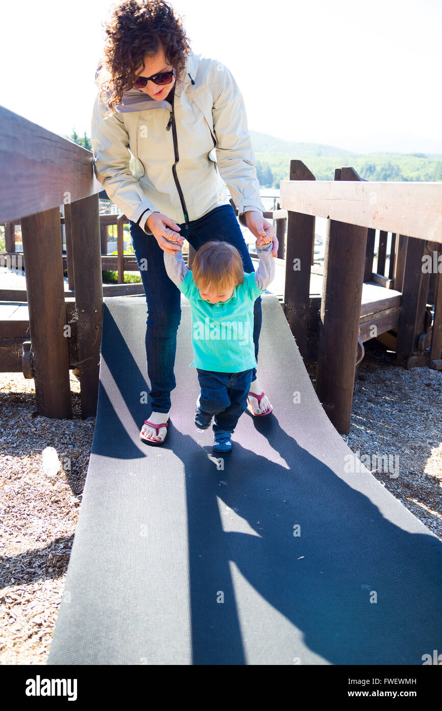 Una madre e suo figlio attraversare un ponte instabile in un parco giochi insieme. Foto Stock