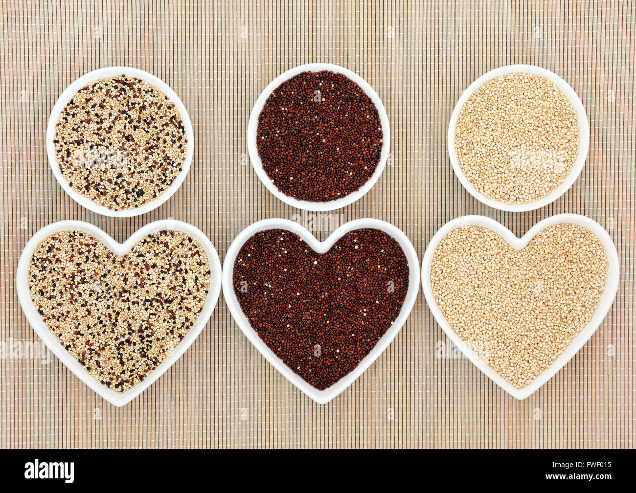 La quinoa salute e super varietà alimentare nel cuore e di forma rotonda ciotole di porcellana su sfondo di bambù. Foto Stock