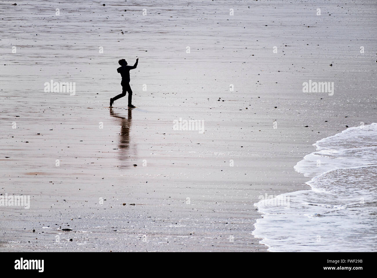 Un giovane ragazzo visto in silhouette e da una distanza che gioca da se stesso su Fistral Beach in Newquay, Cornwall. Foto Stock