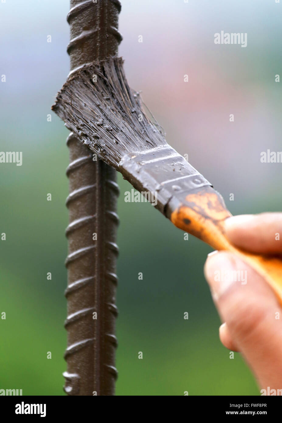 Verniciatura di una bacchetta di ferro con un pennello per esterno Foto Stock