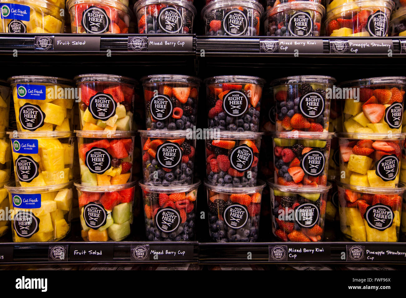 Contenitori di plastica di pronto a mangiare frutta tritato vengono impilati in righe in un contenitore refrigerato in un negozio di alimentari. Foto Stock