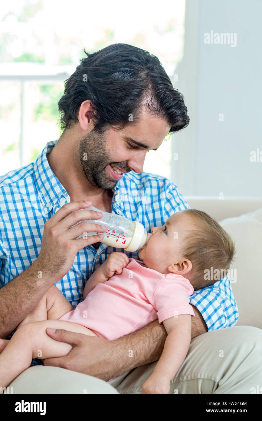 Padre Felice alimentazione di latte al figlio sul divano Foto Stock
