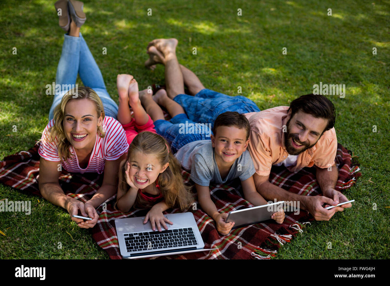 Famiglia sorridente utilizzando tecnologie pur giacendo in cantiere Foto Stock