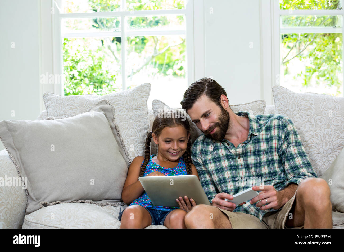 Felice ragazza mostra digitale compressa al padre sul divano Foto Stock
