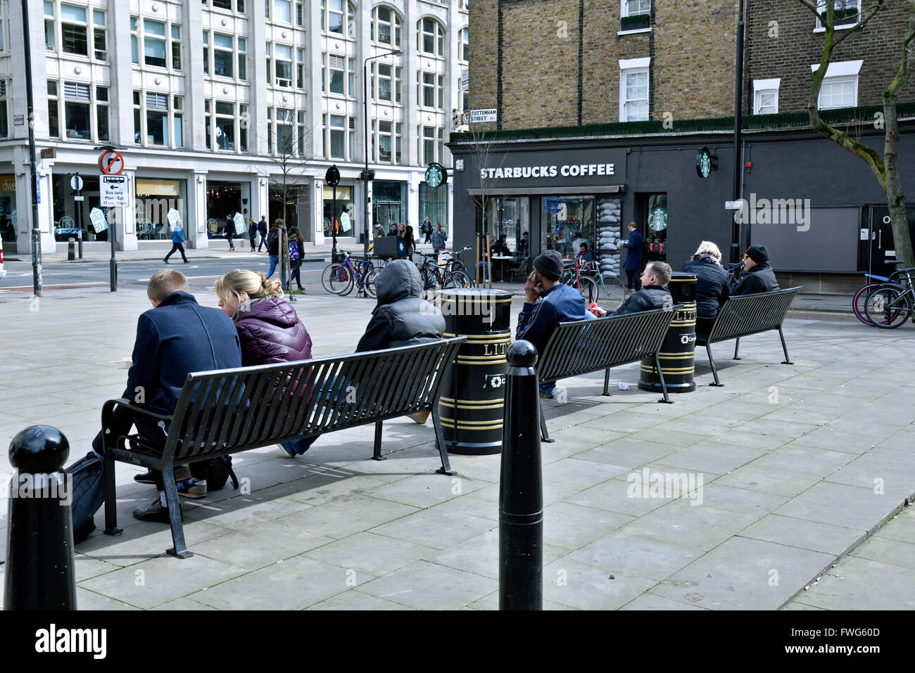 La gente seduta sulle panchine in pubblico spazio aperto oltre Tottenham Court Road, London Borough of Camden Inghilterra Gran Bretagna REGNO UNITO Foto Stock