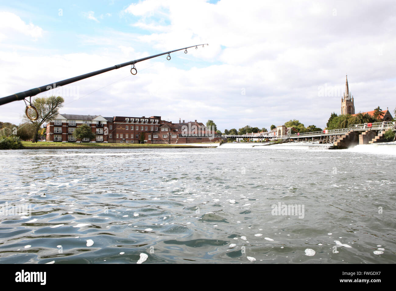 Una canna da pesca e la linea al di sopra di un tratto di acqua da uno stramazzo e il bridge e gli edifici di una città. Foto Stock
