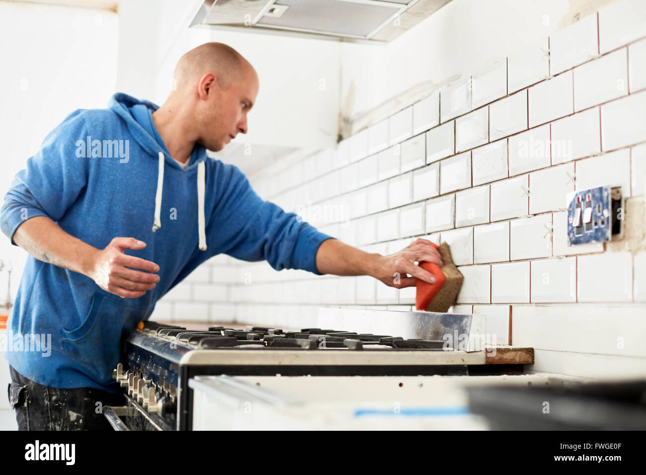 Un uomo che lavora in una cucina nuova, un installatore di piastrelle di applicazione alla parete dietro il fornello. Foto Stock