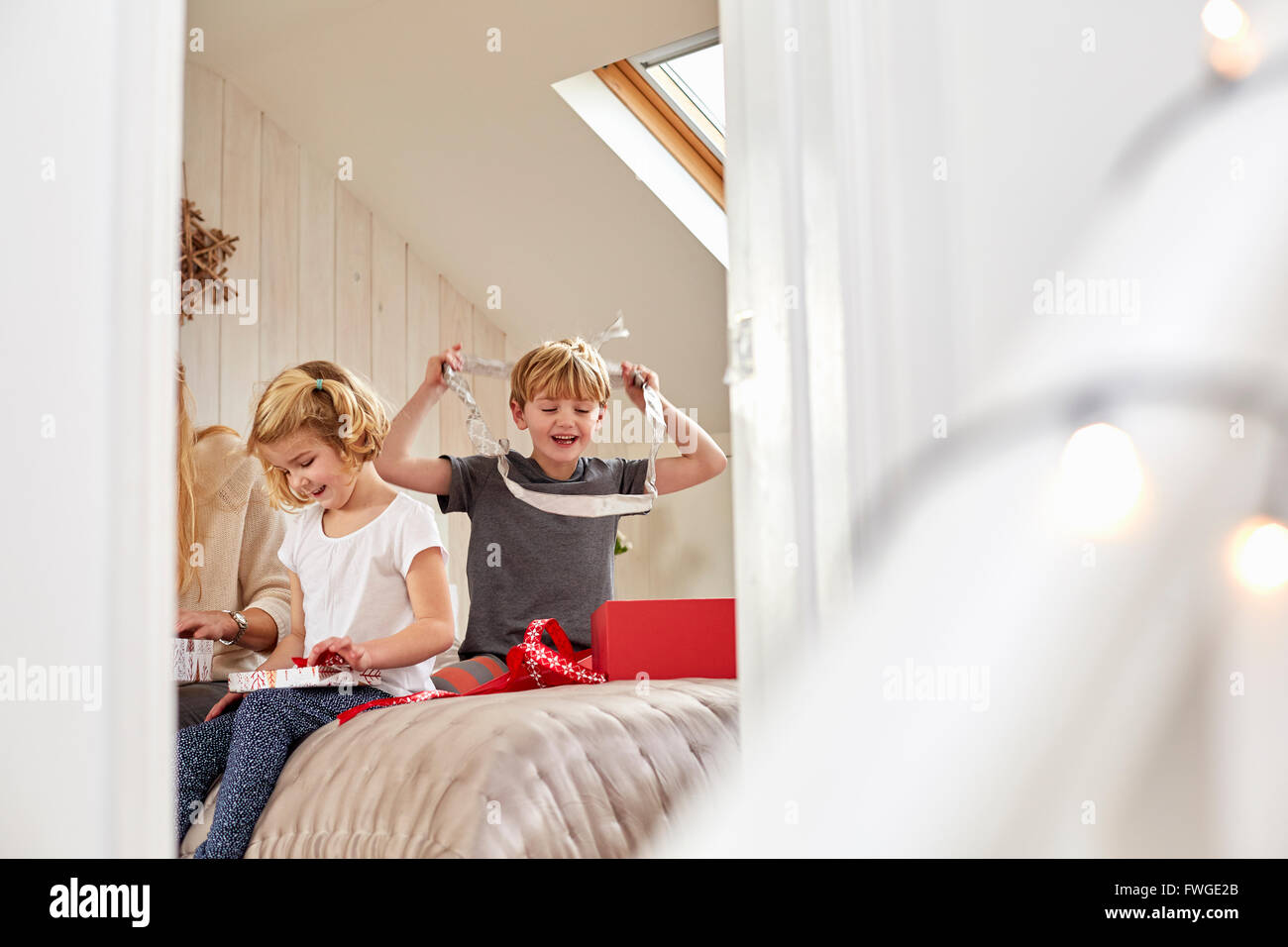 La mattina di Natale in una casa famiglia. Una madre e due bambini seduti su un letto apertura presenta. Foto Stock