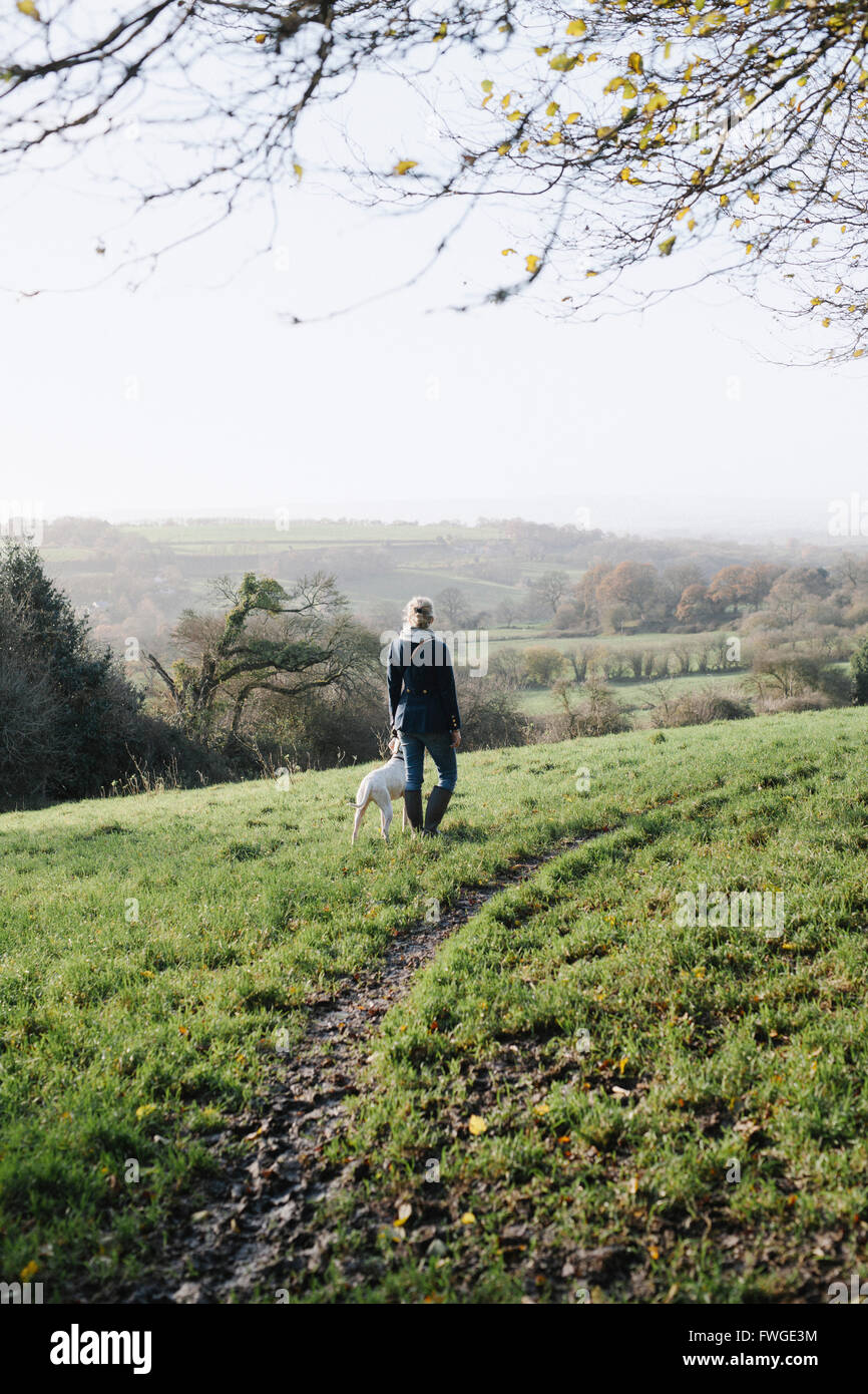 Una donna che cammina con un cane su un terreno elevato che si affaccia sulla campagna. Foto Stock