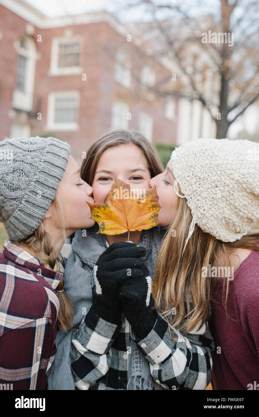 Tre giovani ragazze in piedi in fila uno di trattenere un autumn leaf davanti al suo volto, due bacia sulla guancia. Foto Stock