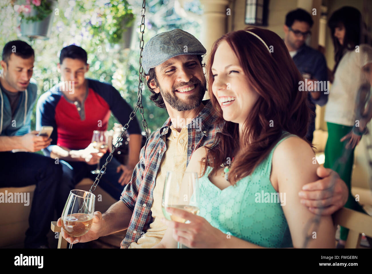Un gruppo di amici, gli uomini e le donne a un house party di bere vino. Foto Stock