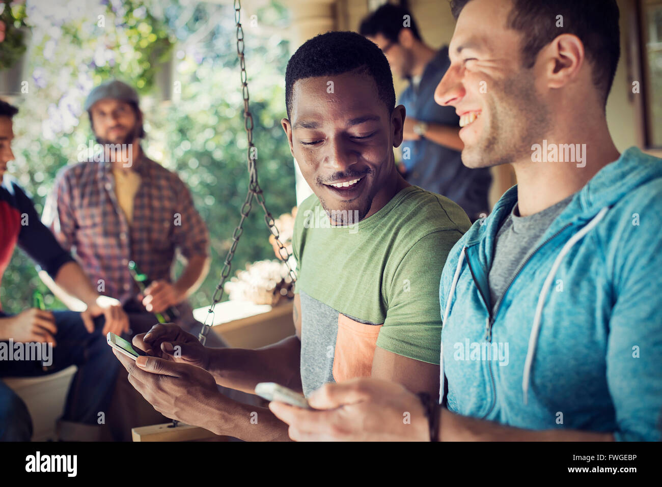 Un gruppo di amici, gli uomini e le donne a un house party, due uomini guardando i loro smart phone. Foto Stock