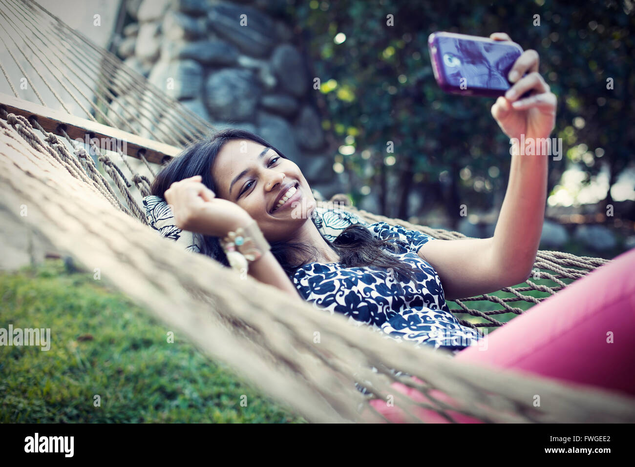 Una donna che giace in un giardino amaca tenendo selfies con il suo telefono cellulare. Foto Stock