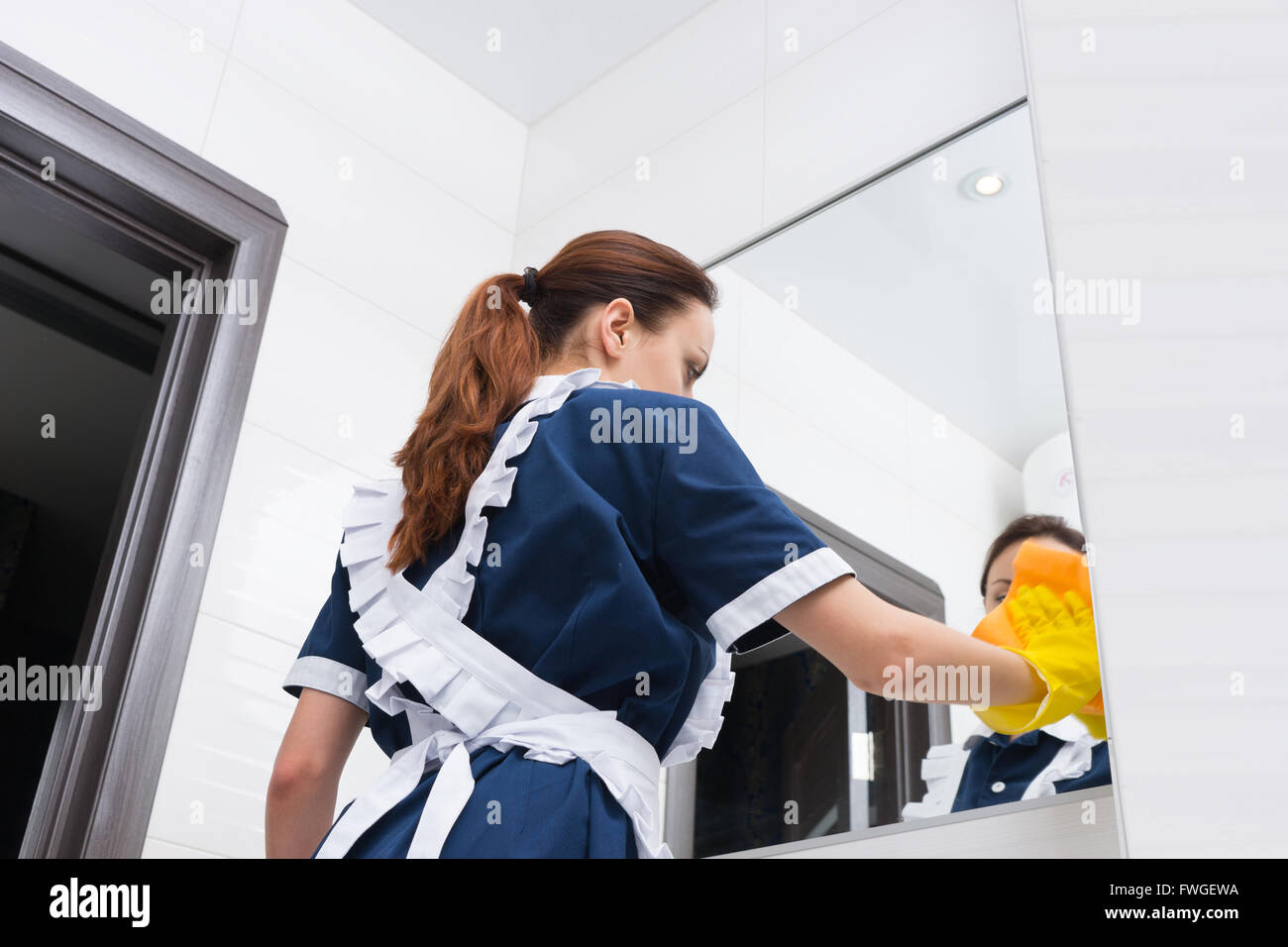 Basso angolo di visione su cameriera in blu e bianco uniforme nei guanti di gomma grande pulizia Specchio bagno Foto Stock