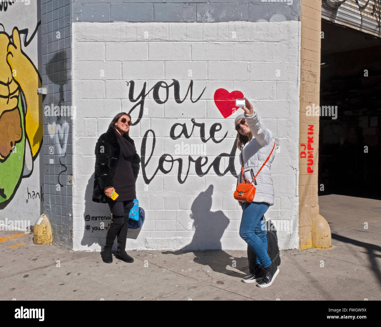 I turisti tenendo selfies davanti a un "Tu sei amato" sulla parete Kenmare St. Angolo di Mulberry in NOLITA, Manhattan New York City. Foto Stock