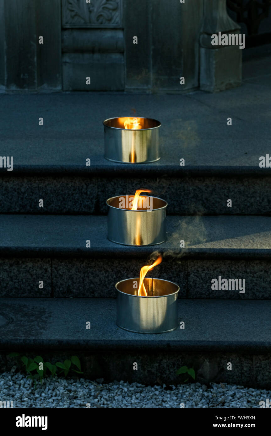 Tre candele accese in metallo forma sui passi nel crepuscolo Foto Stock