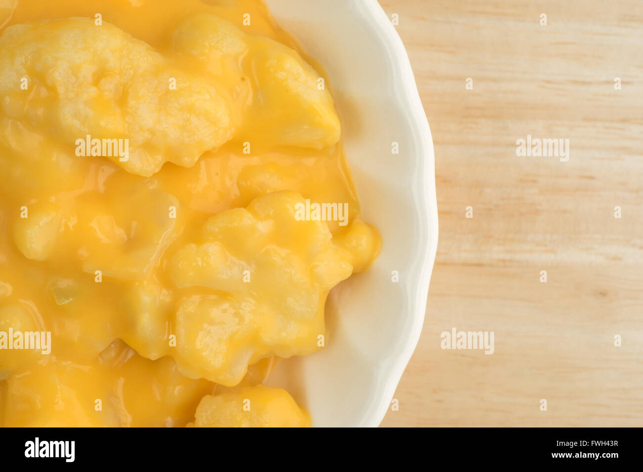 Top vista ravvicinata di un serving di cavolfiore cotta con una salsa al formaggio in una piccola ciotola su una tavola di legno alto. Foto Stock