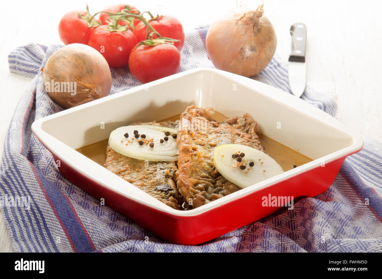 Herringfilet fritto con cipolla, pepe e semi di senape in una ciotola, pomodoro fresco e kitchenknife in background Foto Stock