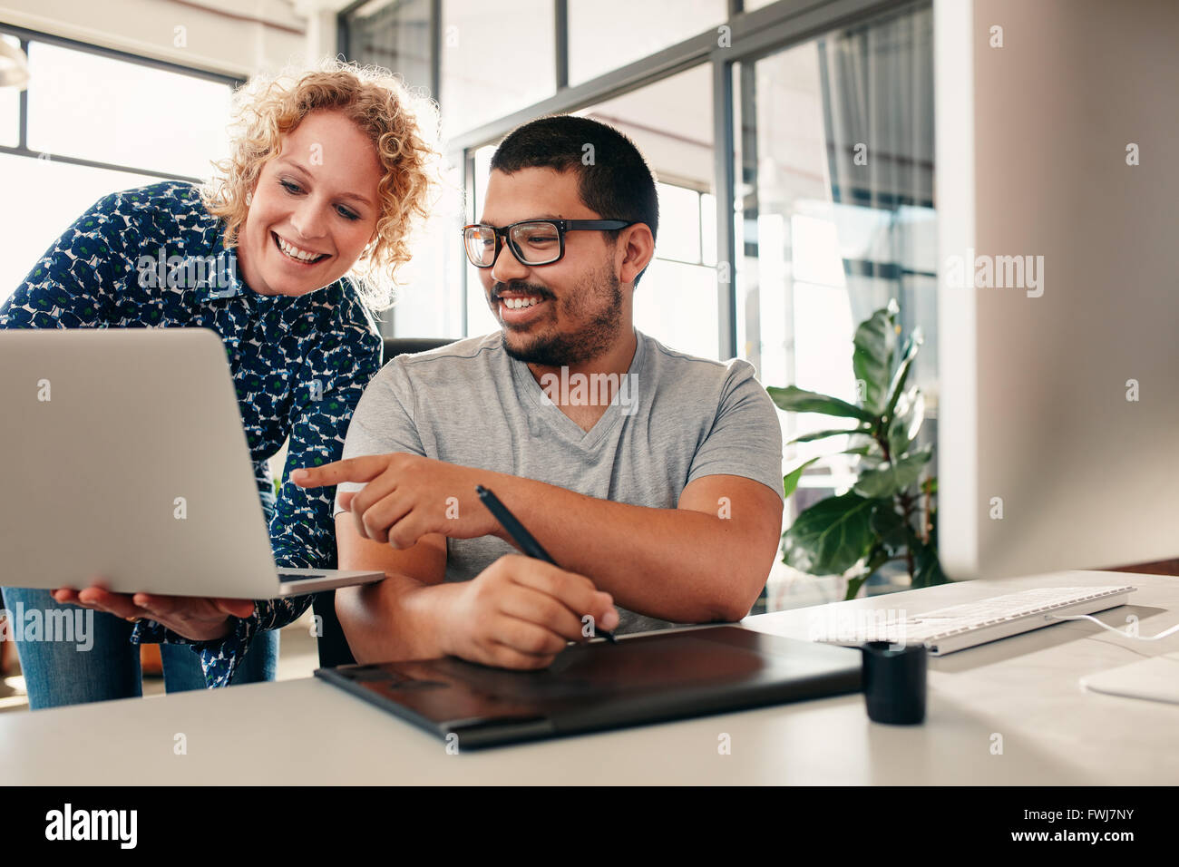 Due giovani graphic designer che lavorano insieme con il collega di sesso femminile che mostra qualcosa di uomo seduto al suo des. Le persone creative di co Foto Stock