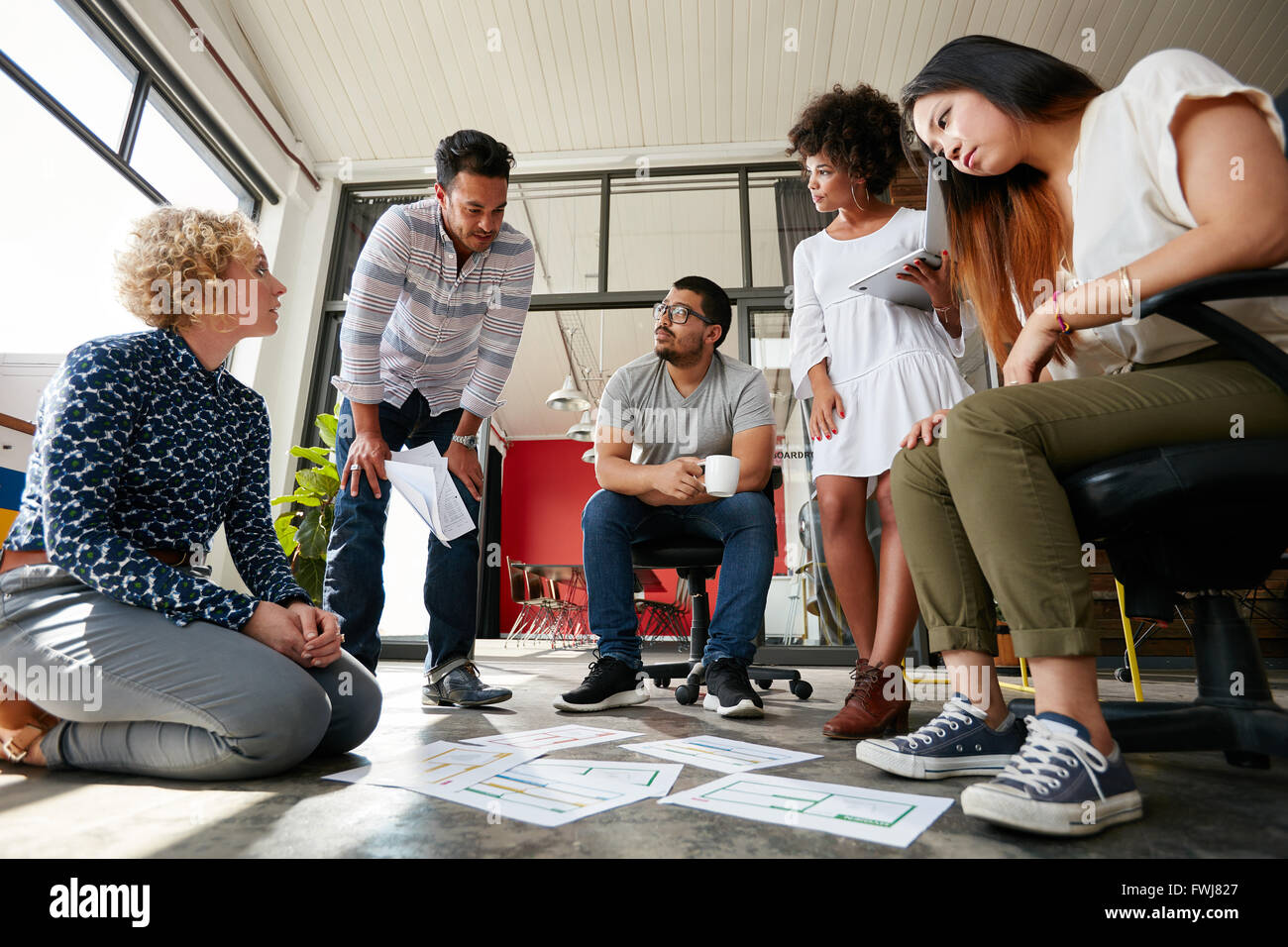 Gruppo di giovani team creative andando su alcuni piani insieme. I documenti di cui fuori sul pavimento con la finalizzazione del design. Foto Stock